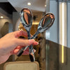 A hand holds a pair of shiny silver spoons against a blurred background.
