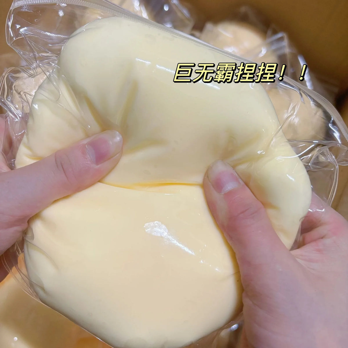 Hände drücken einen großen, blassgelben, weichen Stressball Fidget-Spielzeug in durchsichtige Plastikverpackung.