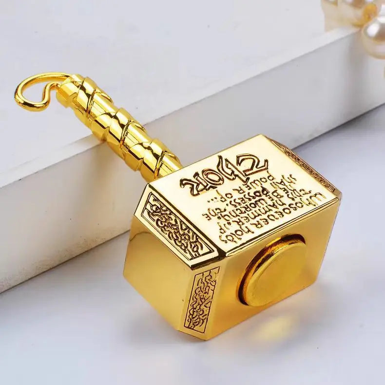 A gold-colored hammer-shaped metal fidget spinner with a transformable design resting on a white surface.