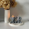 A gray silicone elephant mold sits on a white dish next to a lit candle and dried floral arrangement.