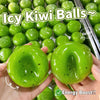 A hand holds a bright green icy kiwi ball stress ball with black spots against a background of many similar balls.
