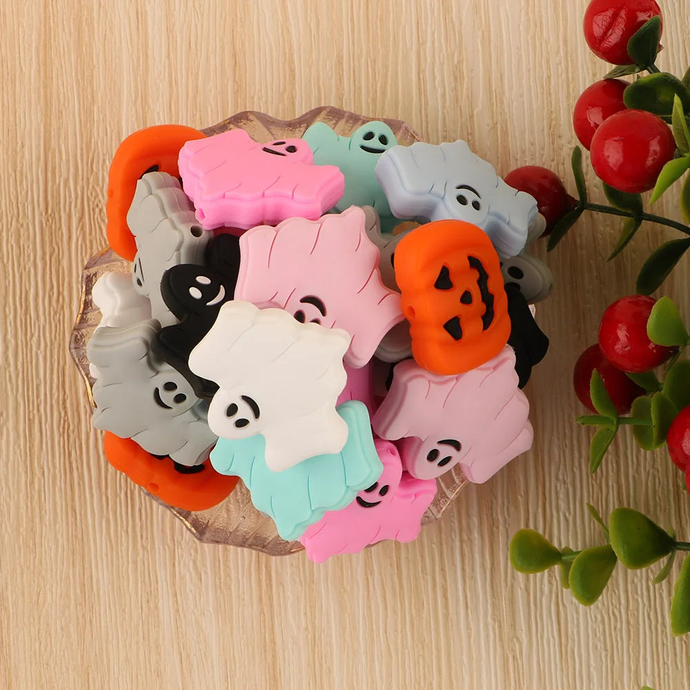 A set of five silicone ghost-shaped beads in various pastel and orange colors arranged on a wooden surface.