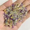 A handful of natural tumbled stone chips in shades of purple, yellow, and clear quartz crystals.