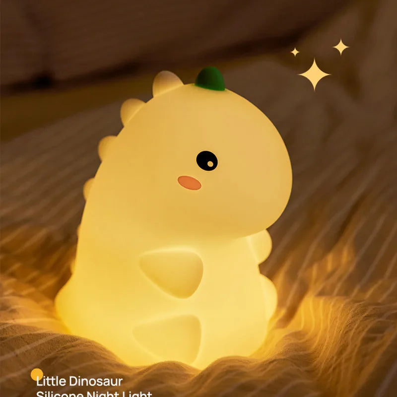 A glowing yellow silicone dinosaur night light resting on a textured fabric.