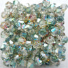A pile of faceted glass bicone beads used for jewelry making, showing various shades of green and clear glass.