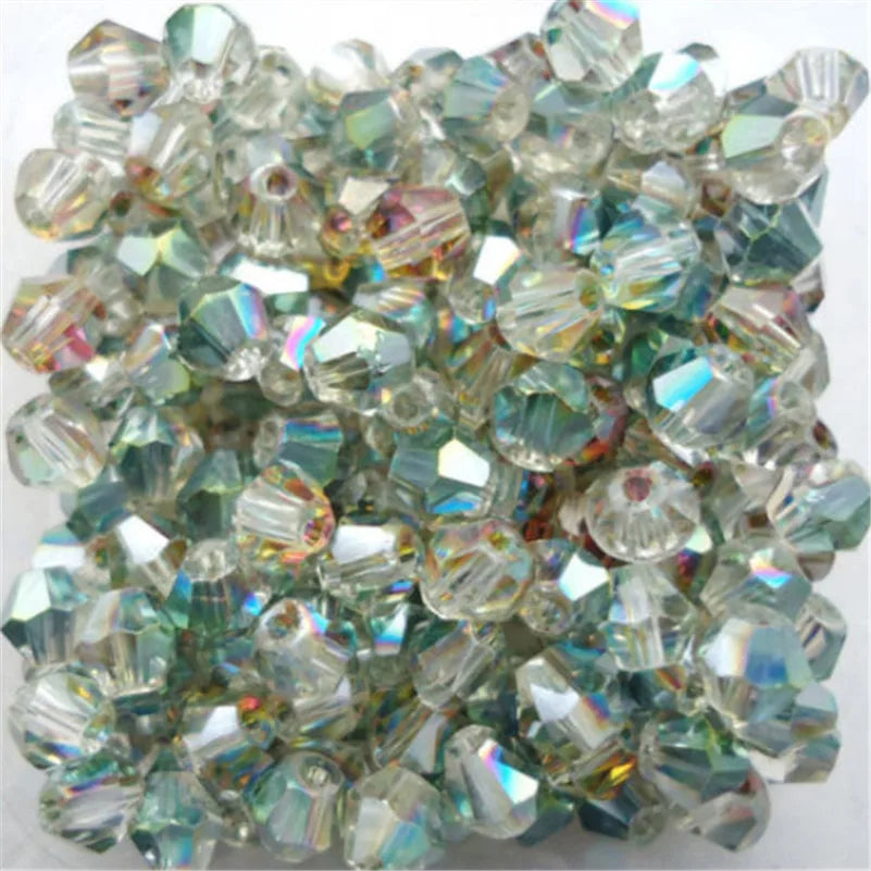 A pile of faceted glass bicone beads used for jewelry making, showing various shades of green and clear glass.