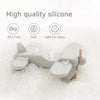 A light gray silicone car teether toy is shown resting on white granular material.