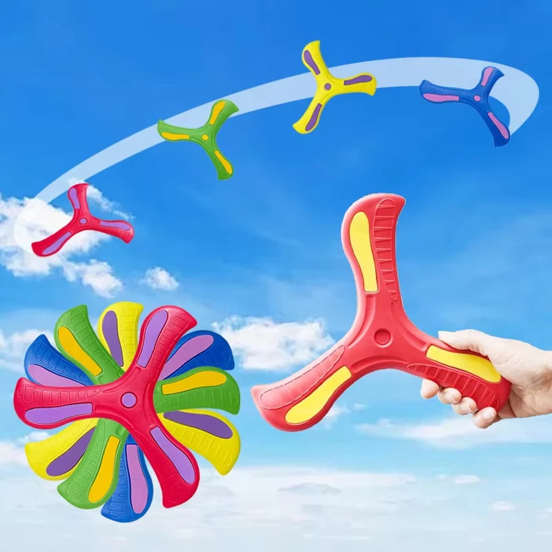 A hand is holding a red soft foam boomerang flying disc, with several colorful discs in flight against a blue sky.