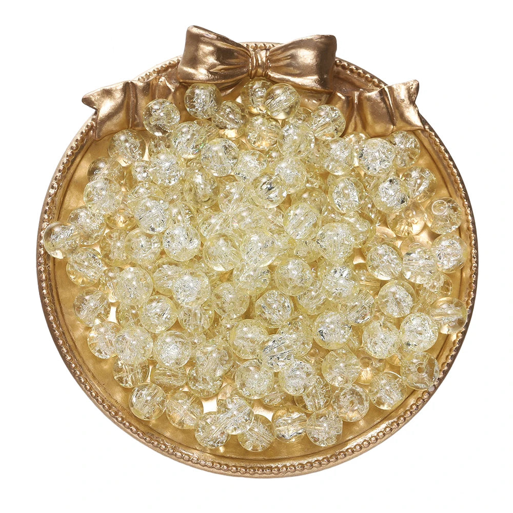 A round gold-toned dish filled with clear glass crackle beads for jewelry making.