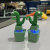 A pair of green duck and frog fidget clickers with LED lights resting on a white surface.