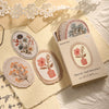 A box of vintage floral stickers with 45 sheets for scrapbooking and journaling displayed on a light fabric.