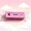 A pink squishy fidget toy labeled GRAPE, measuring 1.6 oz (50g), is displayed against a light pink background with clouds and
