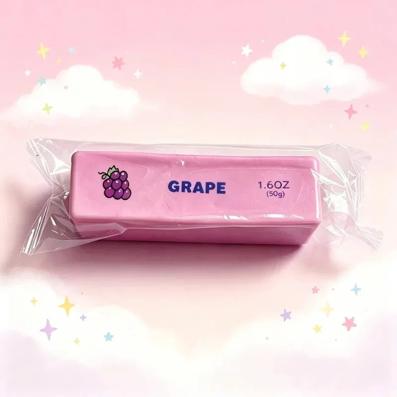 A pink squishy fidget toy labeled GRAPE, measuring 1.6 oz (50g), is displayed against a light pink background with clouds and