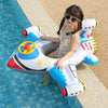 A young girl is sitting in a white and blue inflatable aircraft swim ring on a tiled pool deck.