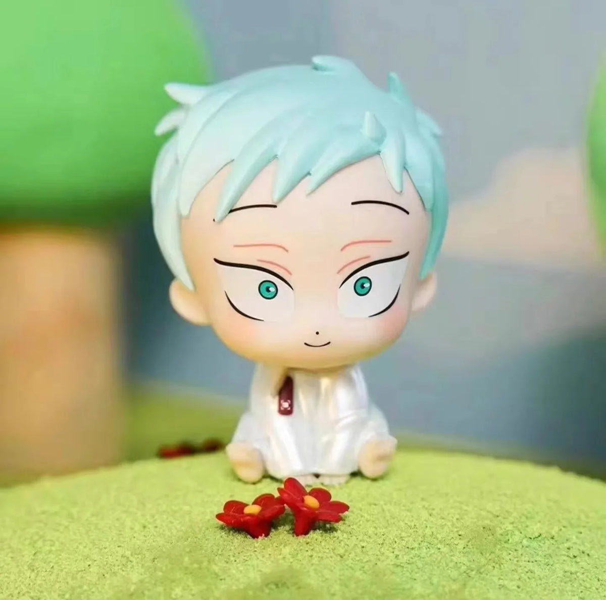 A light blue anime-style mini figure with spiky hair and bright green eyes sitting on a green surface.