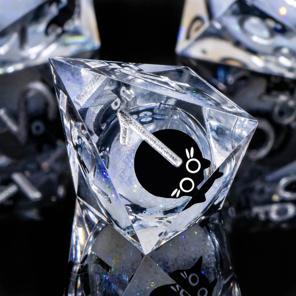 A close-up of a clear, diamond-shaped resin dice set featuring a black cat silhouette.
