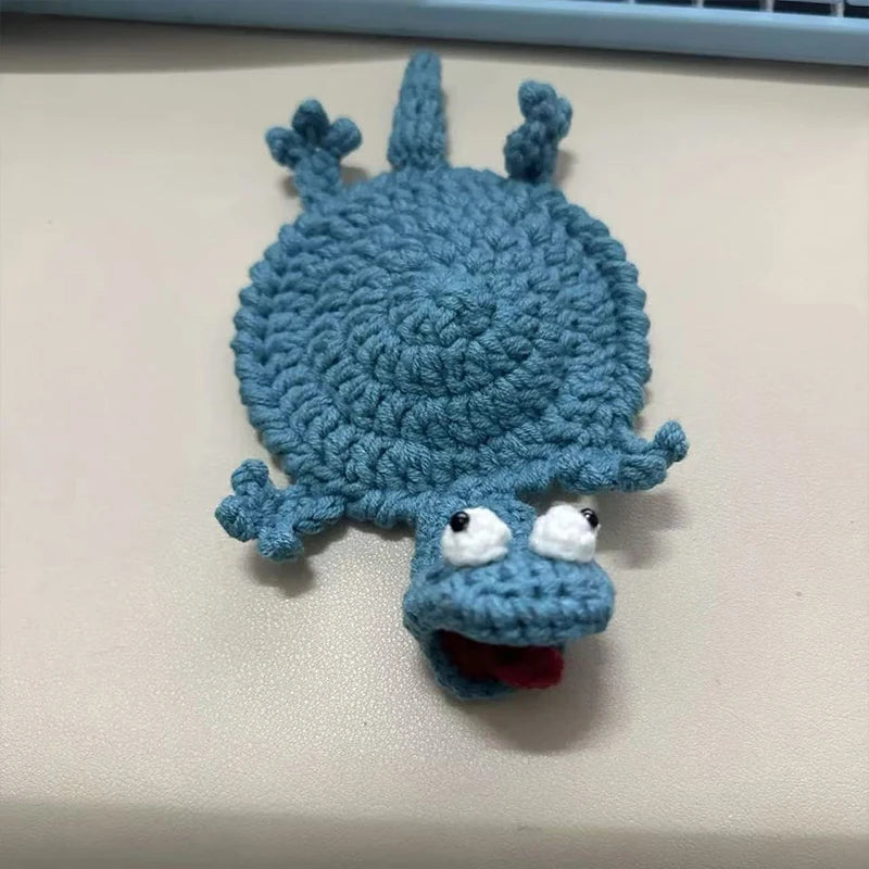 A handmade crochet lizard coaster in blue with a funny expression.