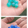 A hand holds a set of seven iridescent, transparent acrylic polyhedral dice on a green background.