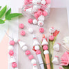 A clear jar filled with pink and white silicone beads for jewelry and crafting, alongside a string of matching beads.
