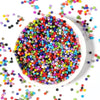 A bowl filled with 24 colors of small glass seed beads for jewelry making and DIY crafts.