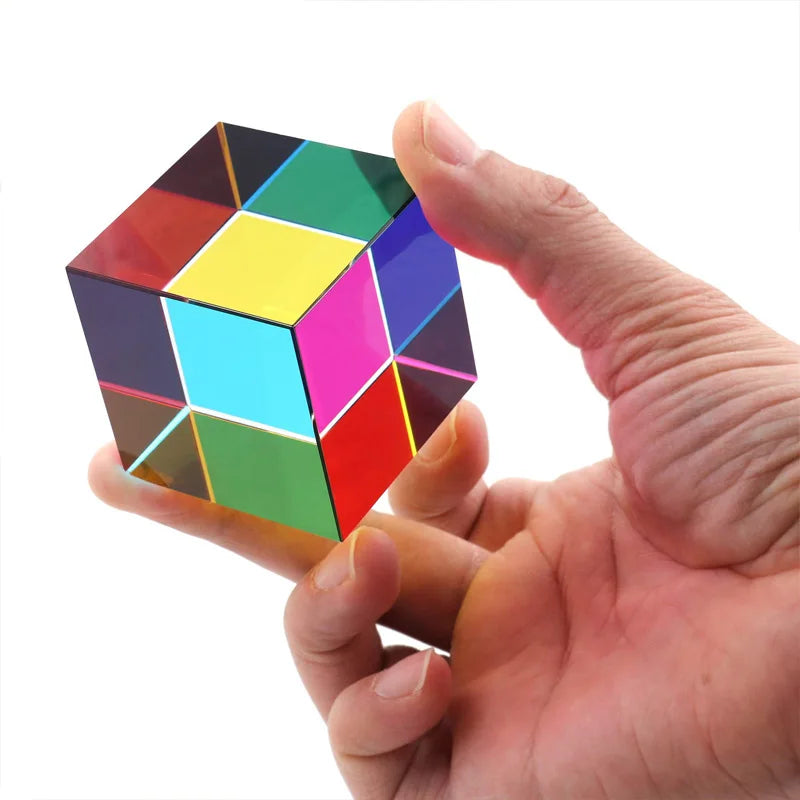 A hand holds an optical color cube prism displaying various vibrant colors.