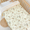 A soft fleece beanie blanket with a light beige pattern is displayed on a wooden crib railing.