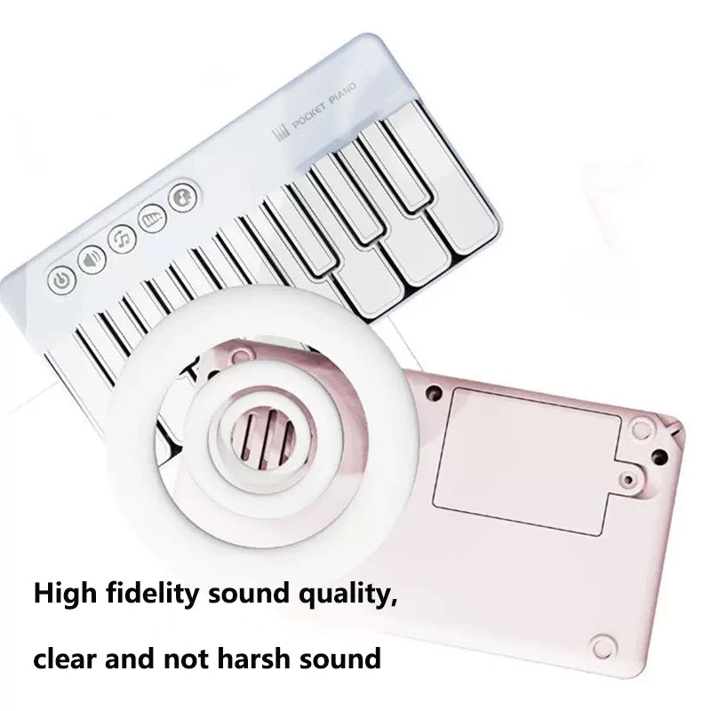 A white mini piano with a pink key cover and a circular accessory shown next to it.