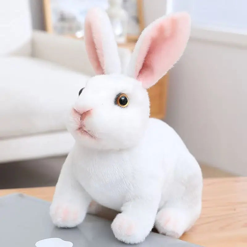 A white plush rabbit toy is sitting on a gray surface.