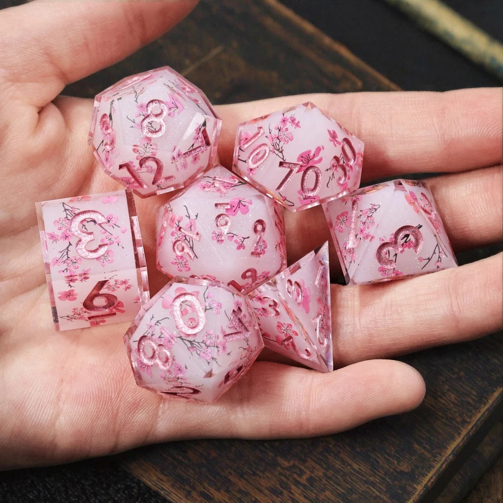 A hand holds a set of pink and white resin polyhedral dice showing numbers like 12, 70, and 6.