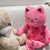 A pink plush rabbit doll with red ears and pink polka dots sitting next to a beige stuffed animal.