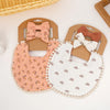 A set of three baby flower bibs and a headband featuring pink, white, and natural fabric textures.