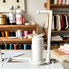 A white vertical sewing machine spool holder with a guide for anti-tangle thread is shown on a white surface.