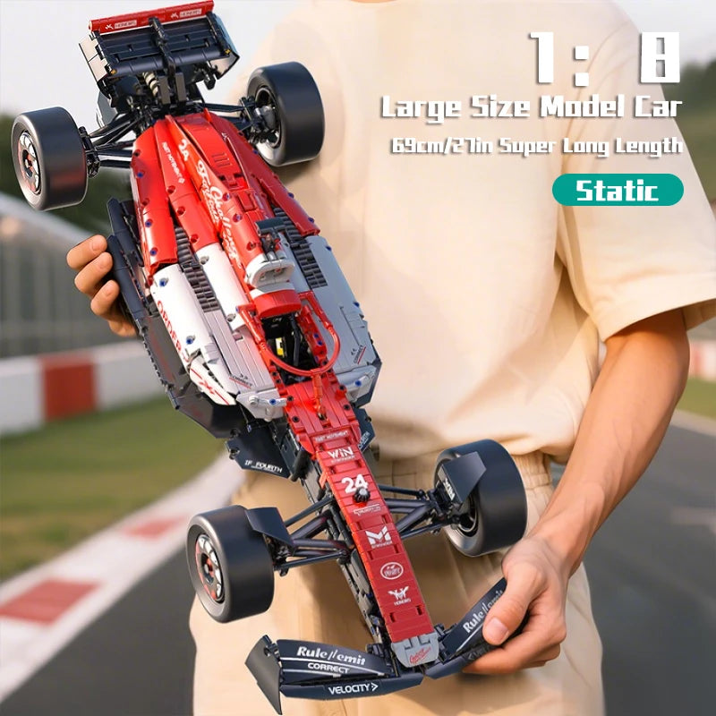 A red 1:8 scale formula racing car model with wheels and linkage is held by a person.