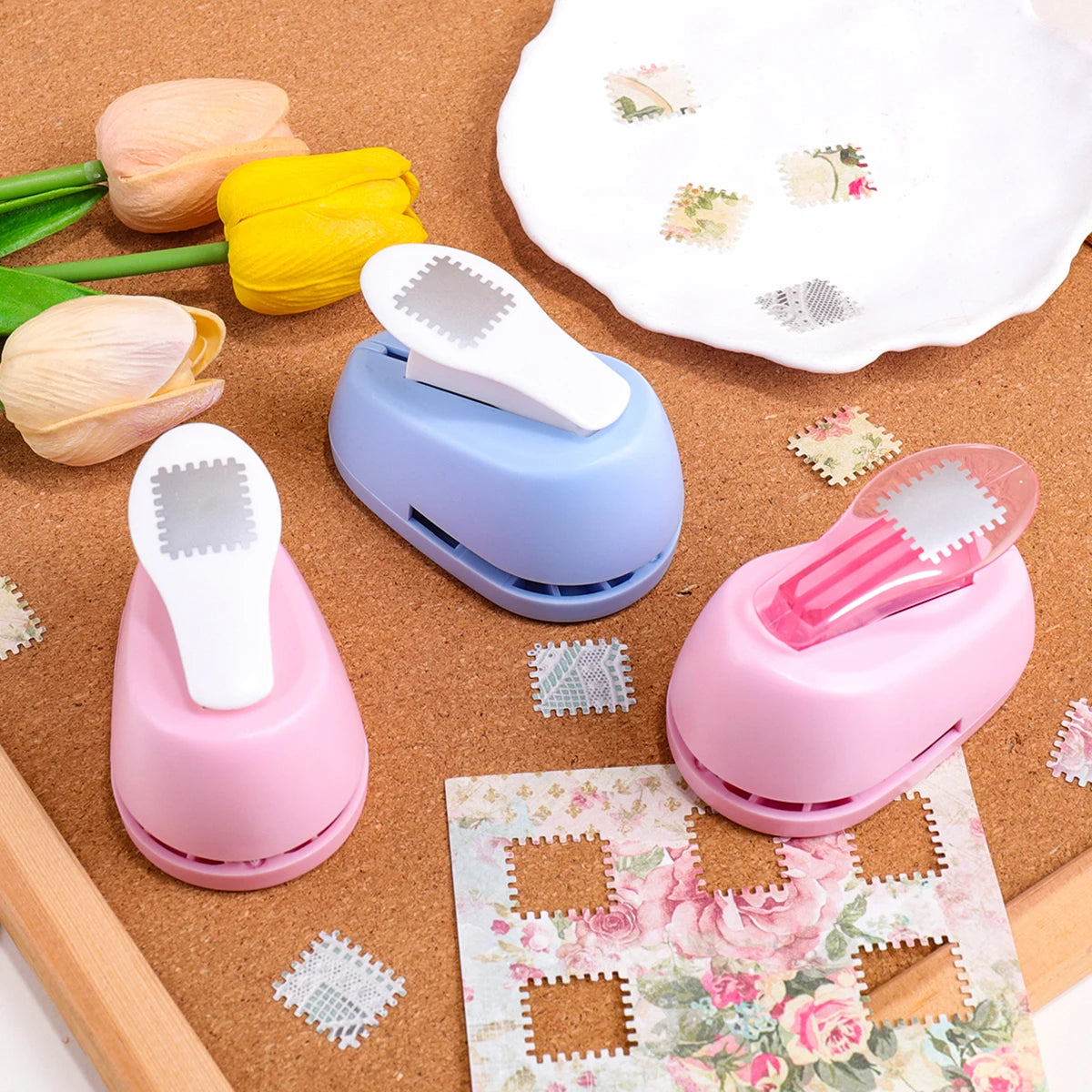 A collection of pink and blue lever action embossers for scrapbooking and card making placed on brown felt with floral paper.