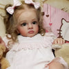 A lifelike reborn baby doll with pink hair and a white dress is shown in a portrait style.