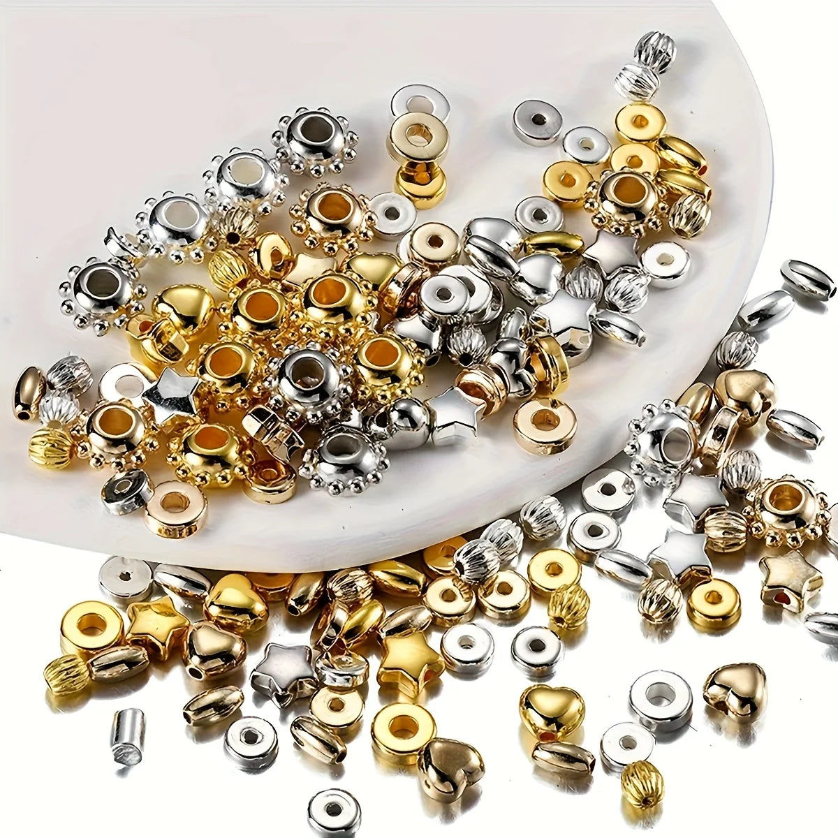 A collection of mixed color acrylic spacer beads in silver, gold, and clear tones scattered on a white surface.