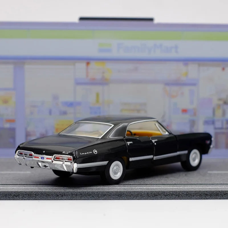 A black diecast model of a 1967 Chevrolet Impala with a yellow interior, displayed on a gray surface.