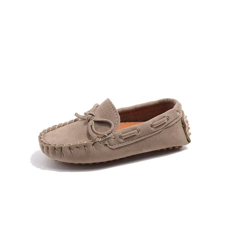 A light tan girls' slip-on moccasin shoe with a bow detail shown from the side.