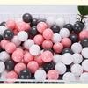 A white plastic basket filled with 50 colorful play balls in shades of pink, black, and white.