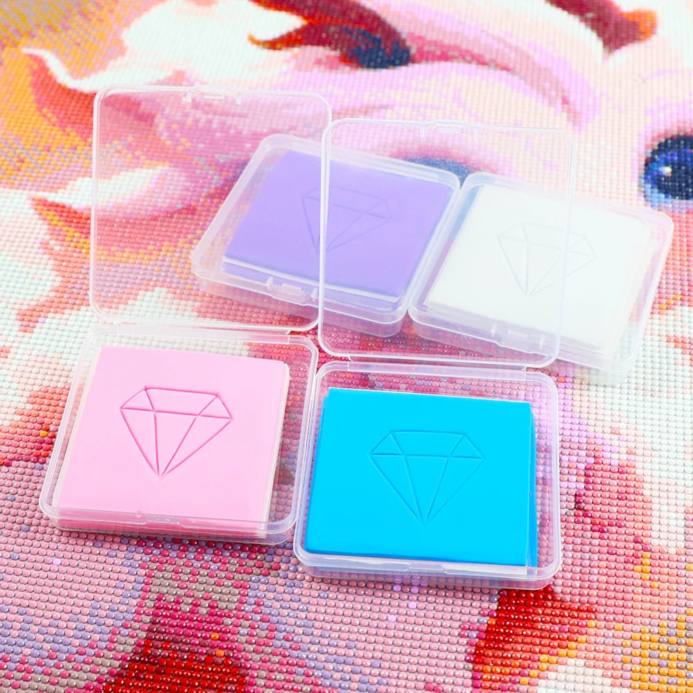 A collection of diamond painting clay in various colors, including pink, purple, and blue, displayed on a textured surface.