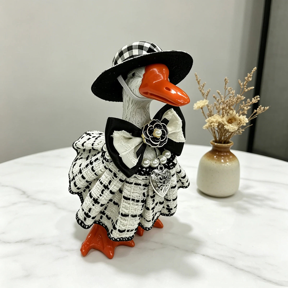 A handcrafted mini goose statue dressed in a black and white plaid dress with a bow and an orange beak.