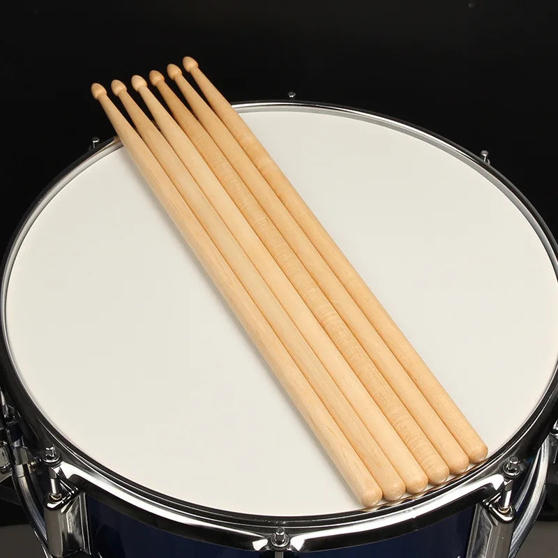 A set of light wood maple drumsticks laid diagonally across a white drum head.