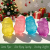 Four colorful squishy figures shaped like Santa heads in yellow, pink, blue, and purple resting on a white surface.