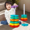A young child is holding a purple stacking tower made of colorful plastic rings on a light-colored surface.