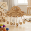 A wooden Montessori busy board for toddlers featuring a spaceship design with hanging sensory elements and gears.