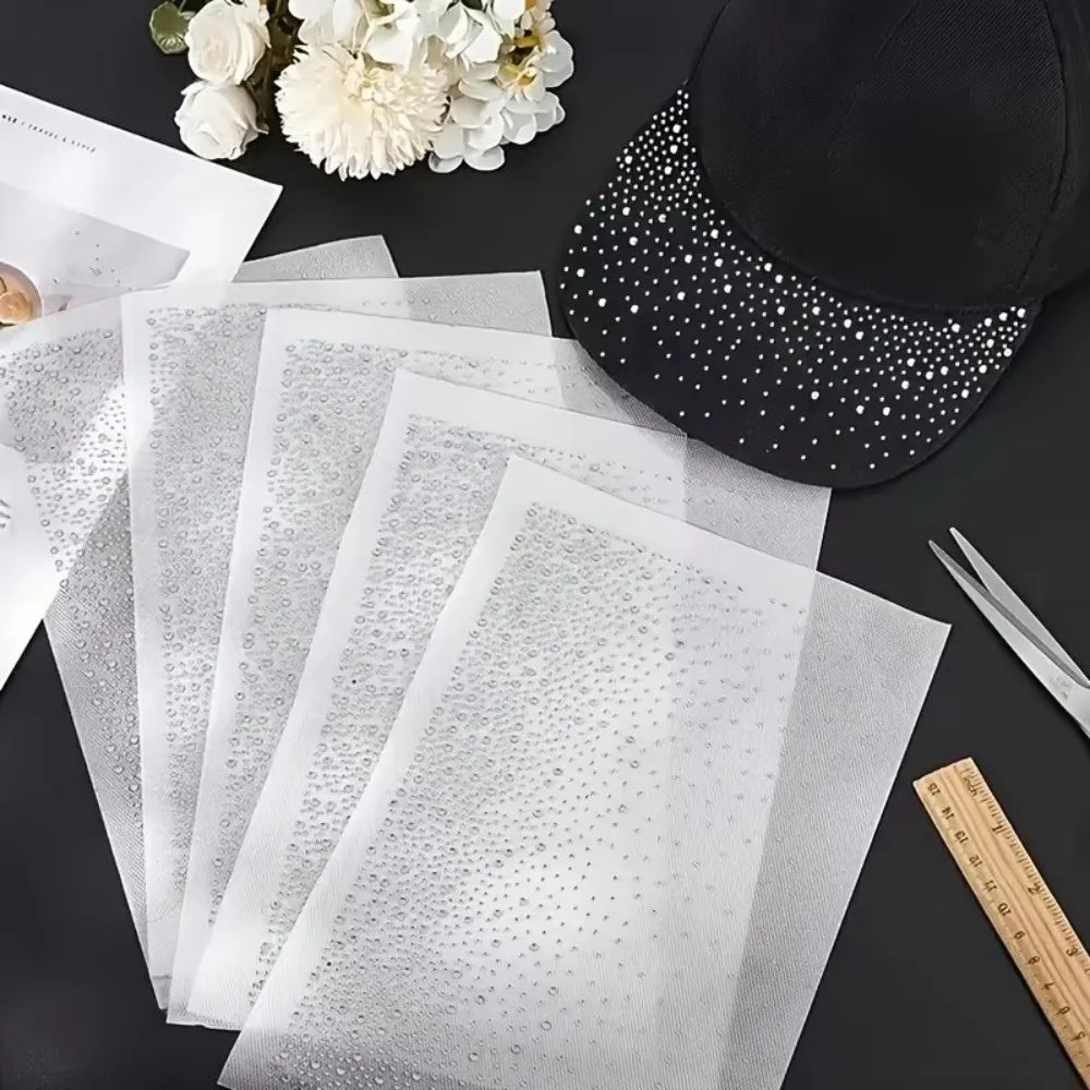 A set of five clear and white gradient polka dot rhinestone sticker sheets next to a black baseball cap.