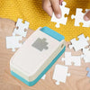 A white and teal DIY puzzle making tool is shown next to several white jigsaw puzzle pieces on a wooden surface.