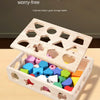 A wooden box storage organizer with various holes and shapes for sorting toys, placed on a light wood surface.