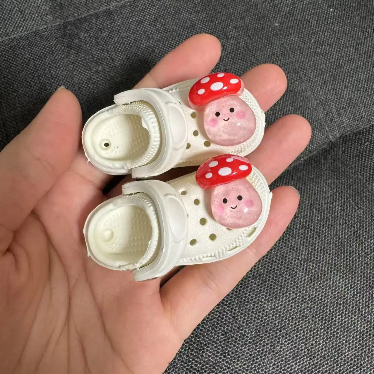 A pair of white fashion slippers for a doll, decorated with pink and red polka dots.
