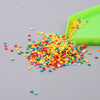 A pile of colorful sequins and small beads spills onto a gray surface next to a green tray.
